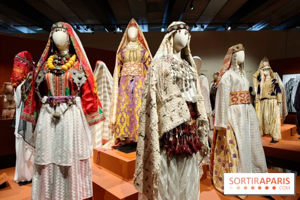 Mannequins habillés de costumes traditionnels colorés et brodés, accompagnés de bijoux, présentés dans une vitrine de l'exposition Vive la mariée ! à l'Institut du monde arabe
