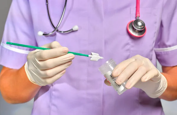 Une professionnelle de santé en tenue violette, stéthoscope autour du cou et gants en latex, tient un écouvillon vert et un petit flacon d'échantillon lors d'un frottis de dépistage du cancer du col de l'utérus.