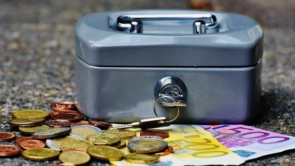 Boîte forte grise métallique avec clé, entourée de pièces et de billets d’euros, illustrant le dépôt de garantie locatif et les difficultés de restitution en cas de litige