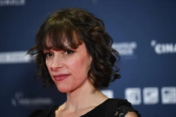 Emily Loizeau, auteure-compositrice-interprète, cheveux courts bruns ondulés avec frange et haut noir, devant un fond bleu avec logos, à l'Institut du Monde Arabe à Paris, le 4 février 2019.