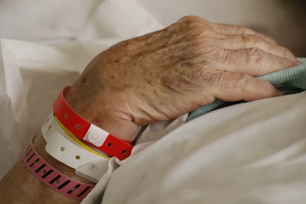Gros plan sur la main d'une personne âgée posée sur un lit d'hôpital, le poignet portant plusieurs bracelets d'identification médicale