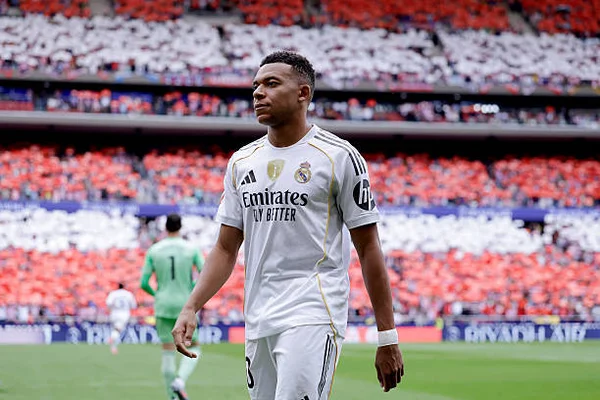 Kylian Mbappé de Real Madrid en action lors du match de LaLiga contre Atlanta Madrid à l'Estadio Civitas Metropolitano, portant un maillot blanc avec des touches dorées, sur un terrain vert avec une foule floue en arrière-plan.