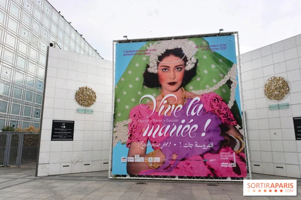 Grand panneau promotionnel de l'exposition « Vive la mariée ! » installé sur un cadre métallique devant l'Institut du monde arabe, aux murs blancs à rosaces dorées