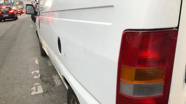 Vue rapprochée de l'arrière d'une camionnette blanche stationnée dans une rue de Paris, montrant son feu arrière et un trou circulaire dans la carrosserie