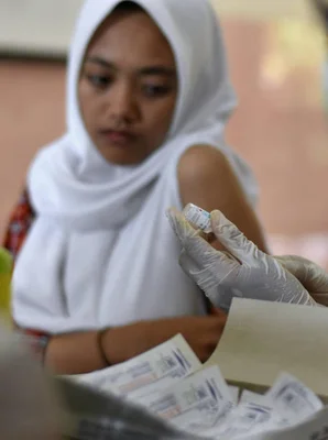 Une femme portant un hijab blanc et des gants blancs manipule de petits sachets au-dessus d'un bac rempli de matériel identique, lors d'une séance de vaccination contre le VPH dans une salle de classe à Malang, à Java oriental, en Indonésie.