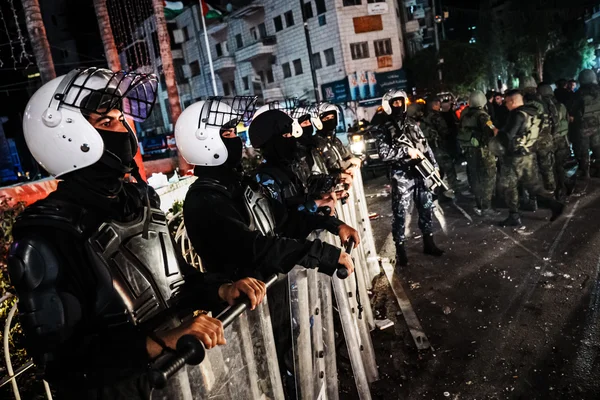 Lignes de forces anti-émeute palestiniennes casquées et masquées se positionnant derrière une barrière métallique la nuit sur la place Al-Menarah à Ramallah en Cisjordanie occupée