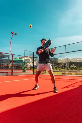 Homme en vêtements athlétiques jouant au tennis sur un court rouge, préparant un coup avec sa raquette.
