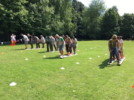 Groupe de personnes en activité d'équipe sur un terrain herbeux, debout sur des planches en bois et tenant des cordes pour coordonner leurs mouvements lors d'une journée sportive d'entreprise.