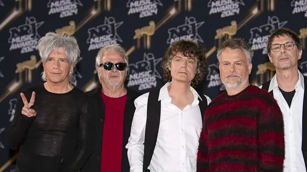 Les cinq membres d'Indochine, dont Marco le bassiste depuis 34 ans, posant en groupe devant le logo des NRJ Music Awards 2024