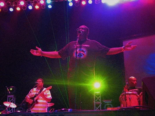 Tabou Combo en concert à Jacmel, Haïti : le chanteur central les bras écartés, un guitariste à gauche et un percussionniste à droite, sous des lumières colorées
