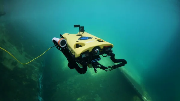 ROV sous-marin jaune équipé d'un bras manipulateur et d'un câble de liaison, immergé dans des eaux bleu-vert lors d'une inspection sous-marine