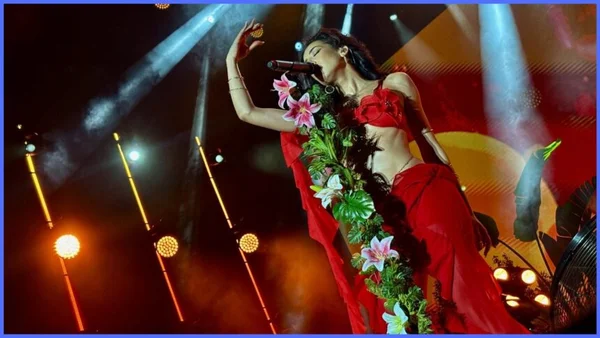 Naïka sur scène au festival Jazzablanca en robe rouge ornée de fleurs, micro à la main et bras tendu, sous les projecteurs scéniques