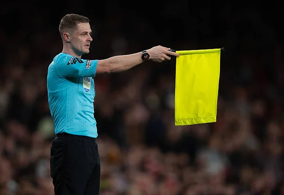 Arbitre assistant portant un maillot bleu clair et un short noir levant un drapeau jaune pour signaler un hors-jeu lors d'un match de Premier League entre Arsenal et Fulham au Emirates Stadium