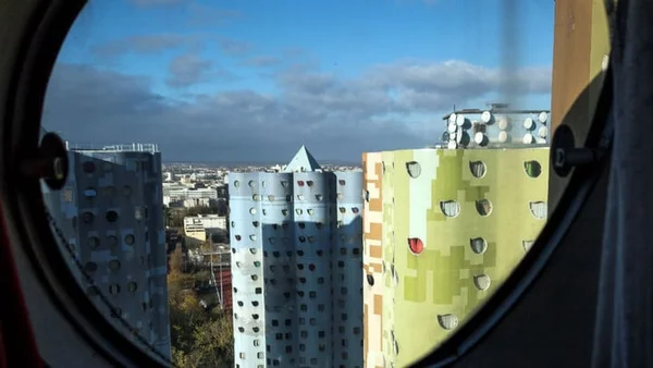 Vue à travers une fenêtre circulaire des Tours Alliaud dites Tour Nuages de Nanterre, immeubles colorés de grande hauteur au design de fenêtres atypique, sous un ciel bleu parsemé de nuages