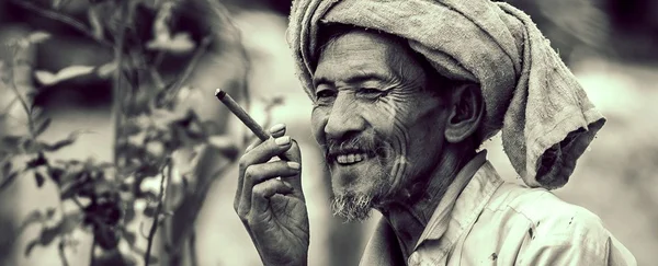Photographie en noir et blanc d'un homme âgé au visage marqué, portant un turban et tenant un cigare, illustrant les fumeurs de longévité