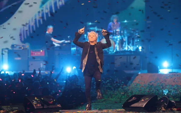 Nicola Sirkis, chanteur d'Indochine, performant sur scène sous un éclairage bleu avec des confettis tombant, entouré des membres du groupe