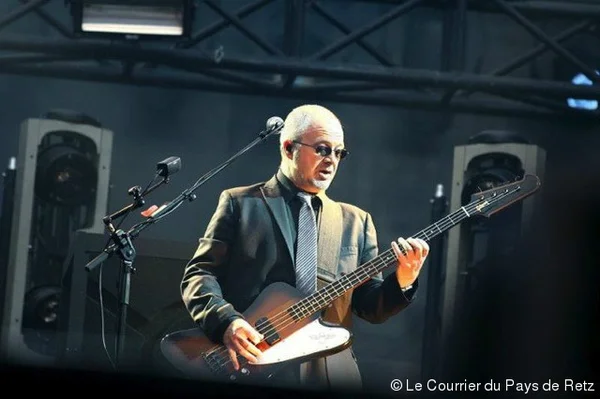 Marc Eliard, bassiste d'Indochine depuis 21 ans, jouant de la guitare basse sur scène en costume et cravate sous les projecteurs