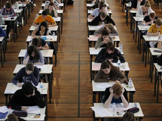 De nombreux étudiants assis à des desks individuels dans un grand hall, concentrés pendant l'examen écrit du baccalauréat français, qui débute avec l'épreuve de philosophie