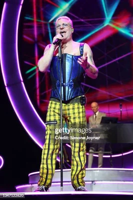 Vince Clarke et Andy Bell d'Erasure en concert sur scène : Andy Bell chante au micro avec des cheveux roses courts, lunettes, corset bleu et pantalon jaune à carreaux