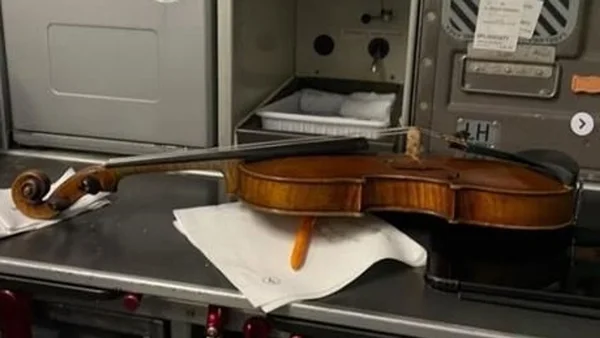 Violon et archet posés sur un tissu blanc sur un plan de travail en inox, avec un étui d'équipement ouvert en arrière-plan, dans le contexte d'un voyage en avion