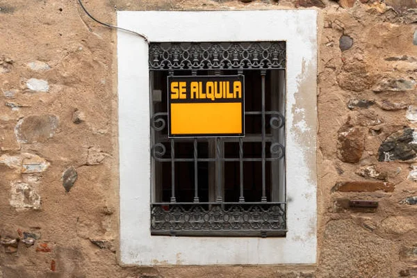 Panneau jaune « SE ALQUILA » (À louer) fixé aux barreaux de fer d'une fenêtre encastrée dans un mur de pierre de la vieille ville de Cáceres, Espagne