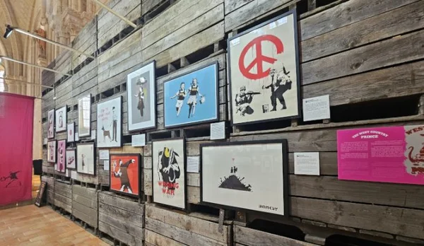 Exposition de presque 300 œuvres de Banksy dans la collégiale Saint-Martin d'Angers : sérigraphies encadrées accrochées à un mur en bois brut avec panneaux explicatifs