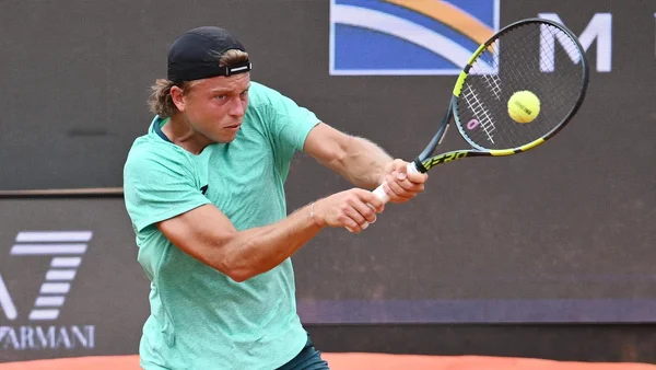 Alexandre Müller, tennisman, frappant un coup de revers à deux mains en revers sur un court de Roland Garros, portant un chapeau noir et une chemise vert clair