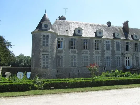 Le château d'Avaray vu depuis l'extérieur, avec sa tour ronde à toit d'ardoise, ses lucarnes et un pont de pierre franchissant un bras d'eau au premier plan