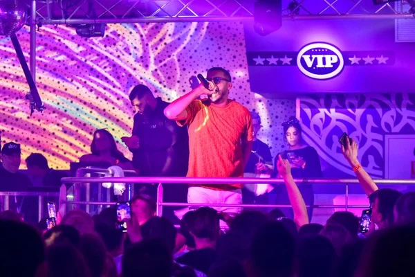 Le rappeur Soso Maness en chemise orange et lunettes de soleil sur scène, micro à la main devant une foule sous les lumières violettes de l'Eldorado à Agen