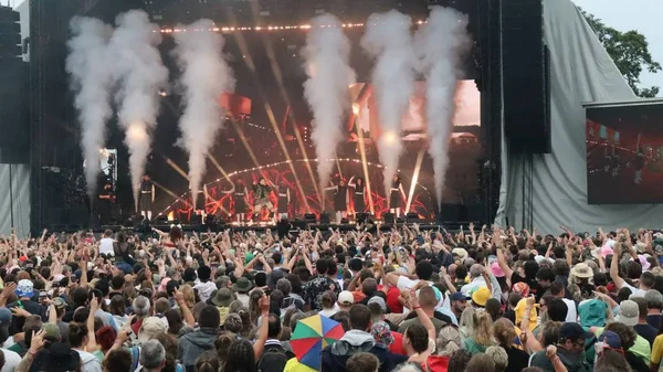 Une foule nombreuse en concert à l'extérieur du festival Art Sonic de Briouze, les bras levés vers la scène éclairée avec des effets de fumée