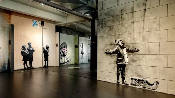 Intérieur du musée Banksy à New York avec des fresques au pochoir sur les murs, dont une œuvre représentant un enfant les bras écartés au premier plan