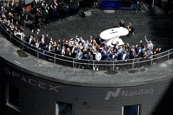 Un groupe de personnes, probablement des salariés SpaceX, rassemblées sur une terrasse surplombant l'événement du Nasdaq, acclament et agitent les mains lors de l'introduction en bourse de SpaceX à New York.