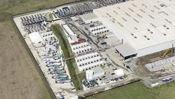 Vue aérienne du data center de xAI à Memphis, avec un vaste bâtiment blanc, des parkings et des zones de stockage extérieur, au cœur de la controverse sur les turbines alimentées au gaz naturel.