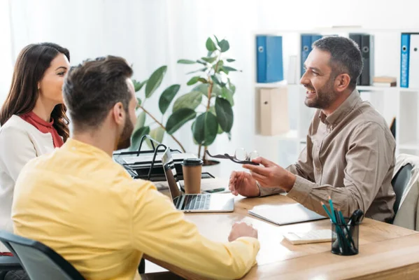 Trois personnes assises autour d'une table en bois dans un bureau, discutant de l'investissement dans des produits structurés en unités de compte d'une assurance vie