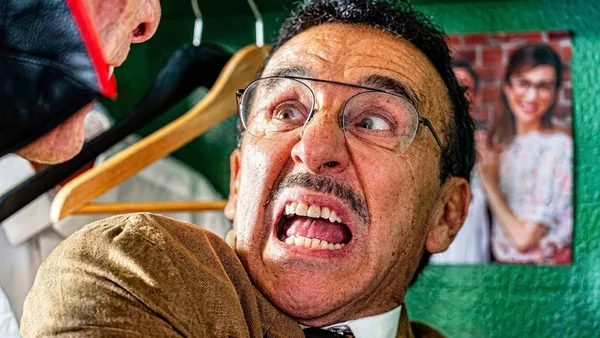 Premier plan d'Elie Semoun dans le rôle de Ducobu, portant lunettes et moustache, expression de surprise, costume marron et cravate, dans un couloir d'école