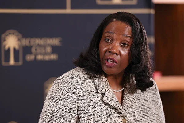 Lisa Cook, gouverneure de la Réserve fédérale, portant un veste texturée et un collier de perles, s'exprimant devant le logo du Economic Club de Miami en février 2026