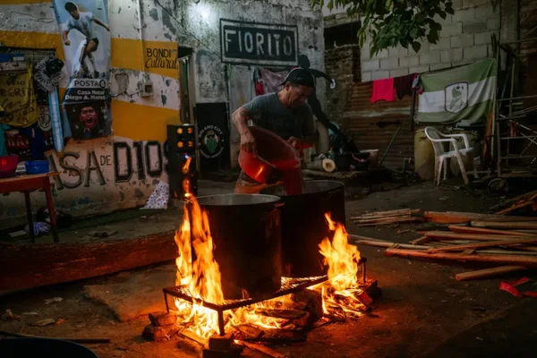 Un homme verse un liquide depuis un seau rouge dans une grande marmite métallique sur feu ouvert, dans la maison d'enfance de Maradona transformée en soupe populaire en Argentine
