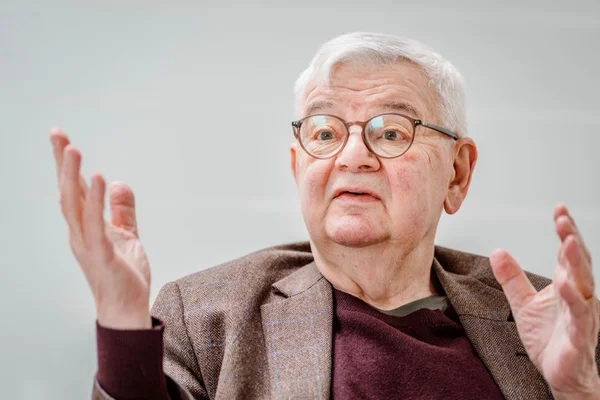 Joschka Fischer, ancien ministre allemand des Affaires étrangères, portant une veste brune sur un pull bordeaux, gesticulant en s'exprimant lors d'un entretien
