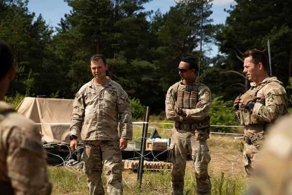 Trois soldats de l'armée américaine en uniforme de camouflage échangeant dans un champ boisé pendant un exercice de tir en Pologne