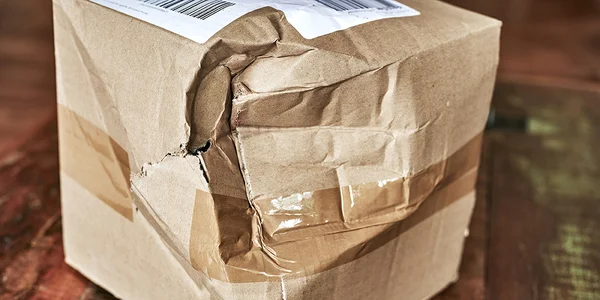 Gros plan d'un colis en carton brun abîmé avec un angle écrasé, scotché et portant une étiquette d'expédition sur le dessus