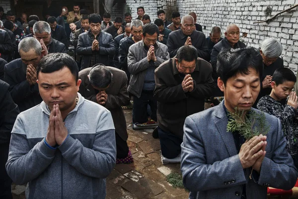Hommes catholiques à genoux et en prière, les mains jointes, dans un lieu de culte en plein air en Chine, contexte de l'église souterraine