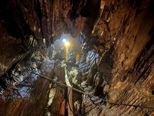 Vue en contre-plongée d'un étroit puits rocheux de grotte au Laos où plusieurs sauveteurs sont rassemblés près d'une source lumineuse vive, des cordes et du matériel de secours visibles au premier plan
