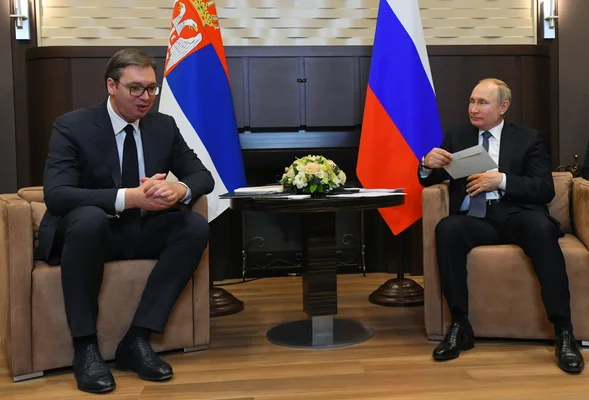 Le président serbe Aleksandar Vučić et le président russe Vladimir Poutine assis face à face lors d'une rencontre officielle, les drapeaux de la Serbie et de la Russie se dressant derrière eux