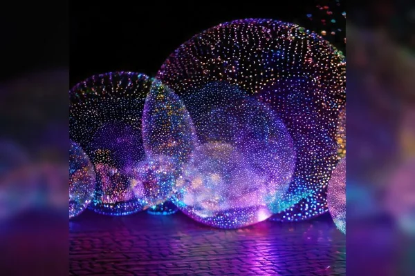 Sphères transparentes couvertes de petites LED multicolores créant un effet bulle lumineuse sur un sol texturé aux reflets violets, bleus et roses pendant la Nuit Blanche à Paris