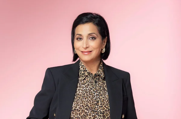 Portrait de Sofia Morgavi, professeure de chant de la Star Academy, portant une veste noire sur chemise léopard, souriant devant un fond rose