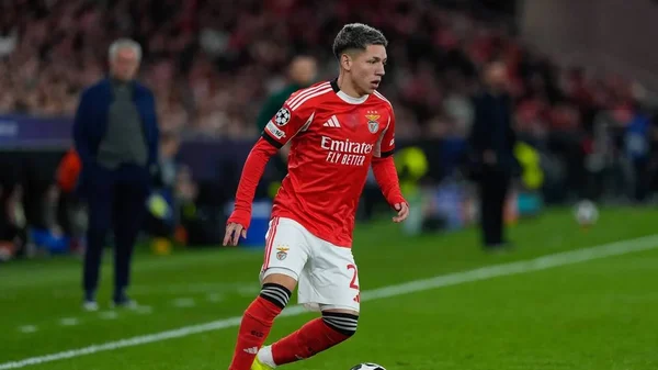 Prestianni, footballeur du Benfica Lisbonne, en maillot rouge et short blanc, dribblant le ballon sur un terrain vert devant les spectateurs des tribunes