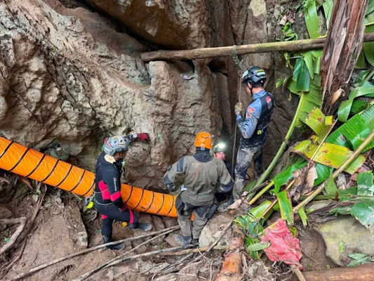Des sauveteurs équipés de casques et de tenues techniques se rassemblent à l'entrée d'une grotte rocheuse dans la province de Xaisomboun, au Laos, avec un large tube de ventilation orange s'engageant dans l'ouverture
