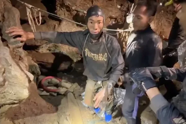 Un plongeur portant une combinaison noire et un bonnet de plongée regarde vers la caméra au milieu d'un groupe de sauveteurs à l'intérieur d'une grotte sombre et inondée au Laos