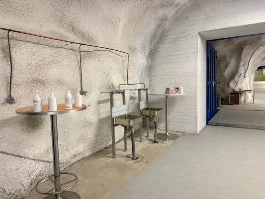 Intérieur fonctionnel d'un abri antiatomique souterrain à Helsinki : murs blancs, deux lavabos en acier inoxydable, une table ronde et une porte bleue métallique donnant sur une autre pièce