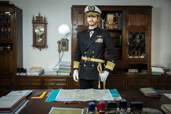 Jonas Lauwiner en uniforme d'officier de marine derrière un bureau, une carte étalée devant lui dans un cadre administratif